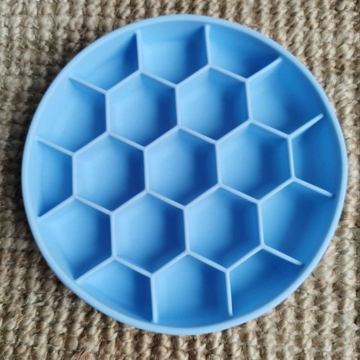 Blue silicone honeycomb enrichment slow feeder bowl on a textured surface