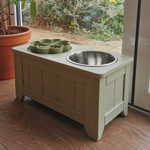 handmade wooden Pet feeding station with metal and enrichment  bowls on a wooden floor, garden visible through glass door.