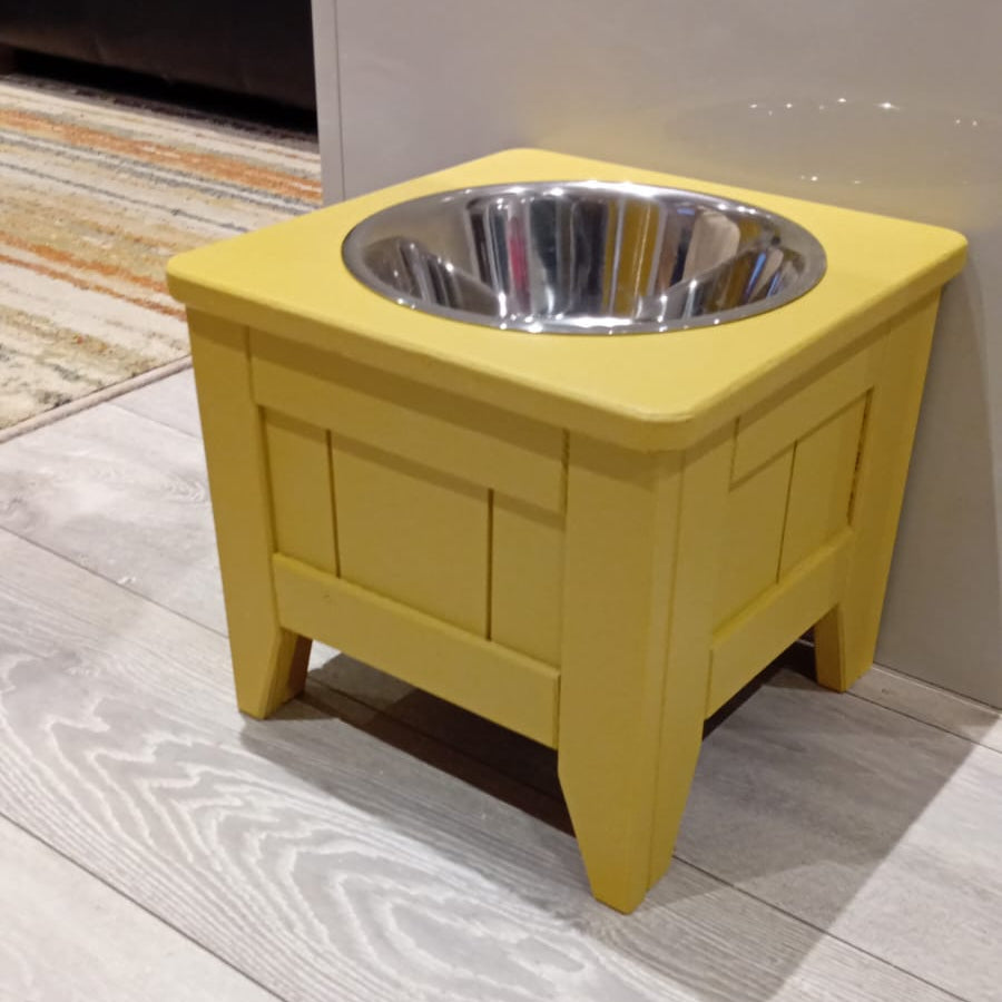 Yellow pet bowl stand with a silver bowl on a wooden floor.