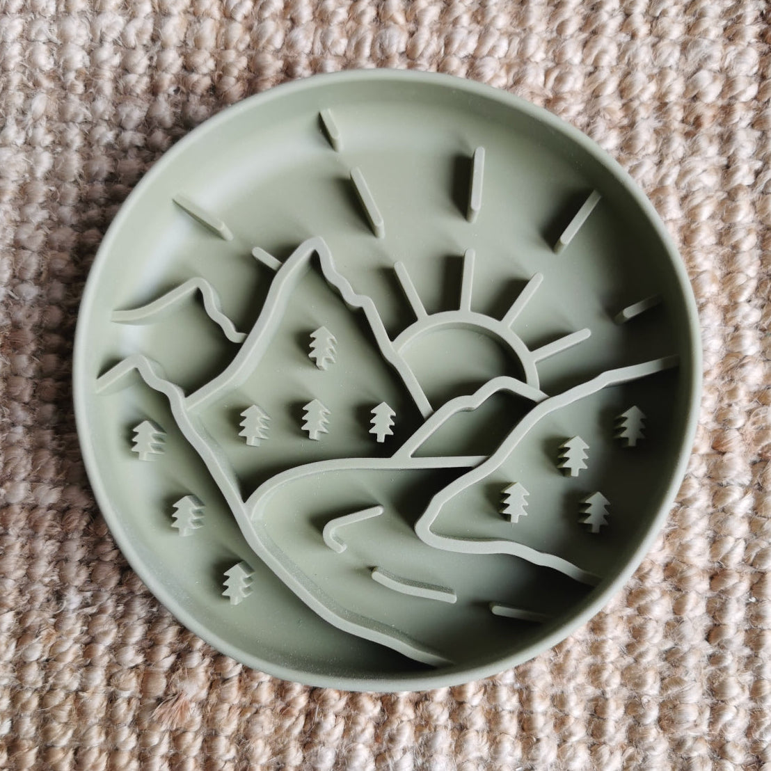 Sage green enrichment bowl with mountain and sun design on a textured beige surface