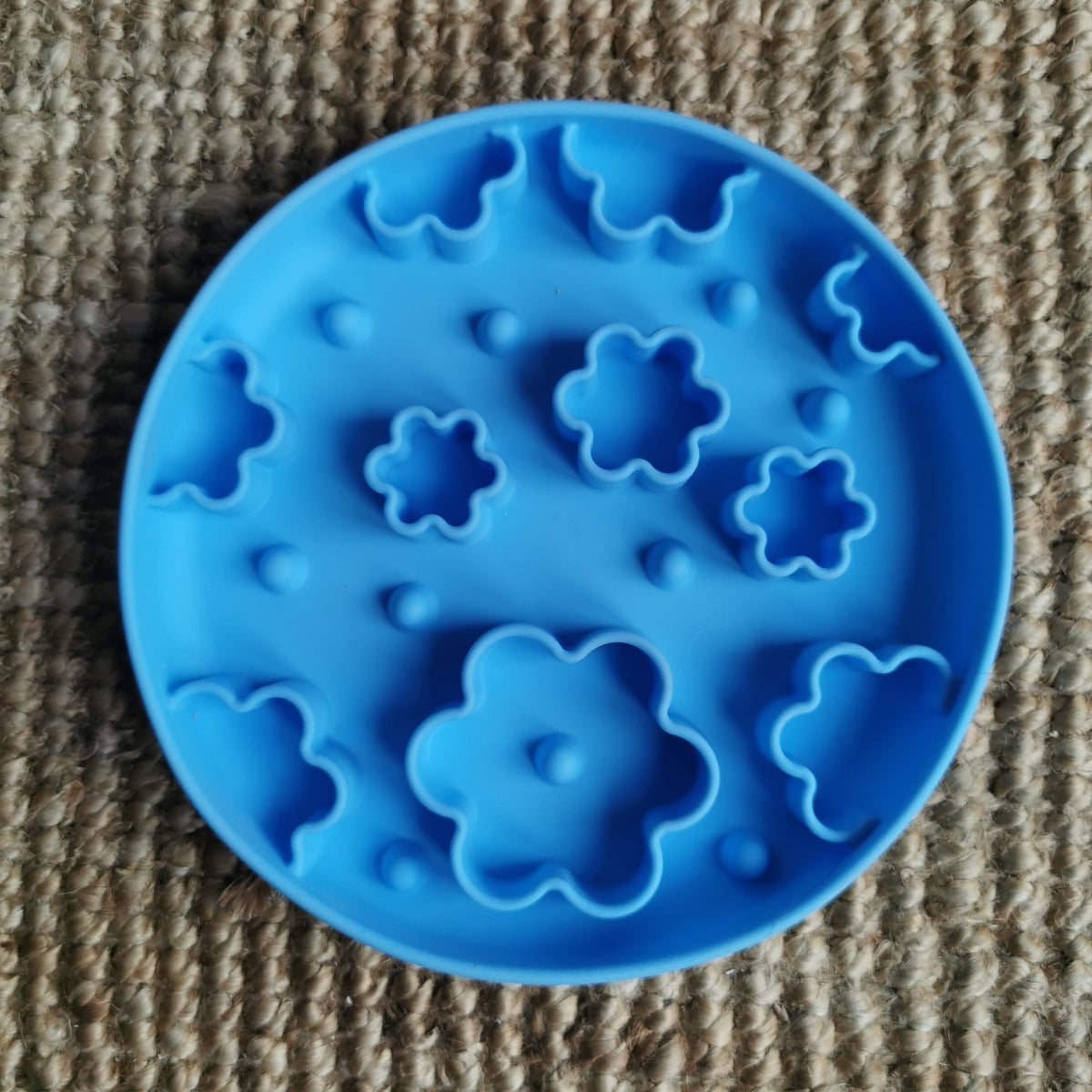 Blue silicone enrichment bowl with floral shapes on a textured brown surface