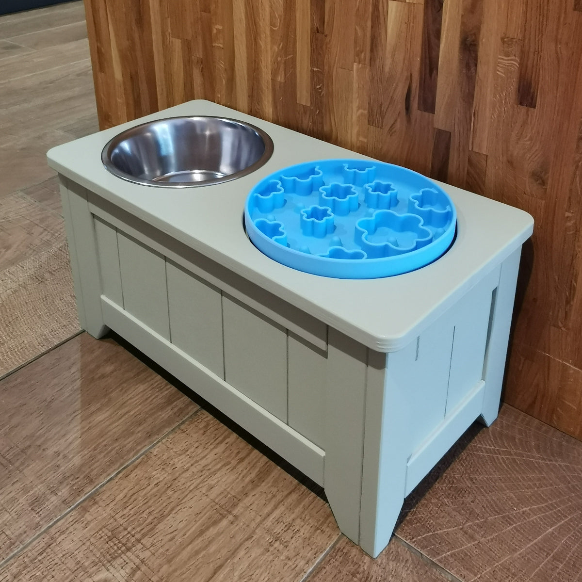 Pet feeding station with a bowl and a blue puzzle feeder against a wooden wall.