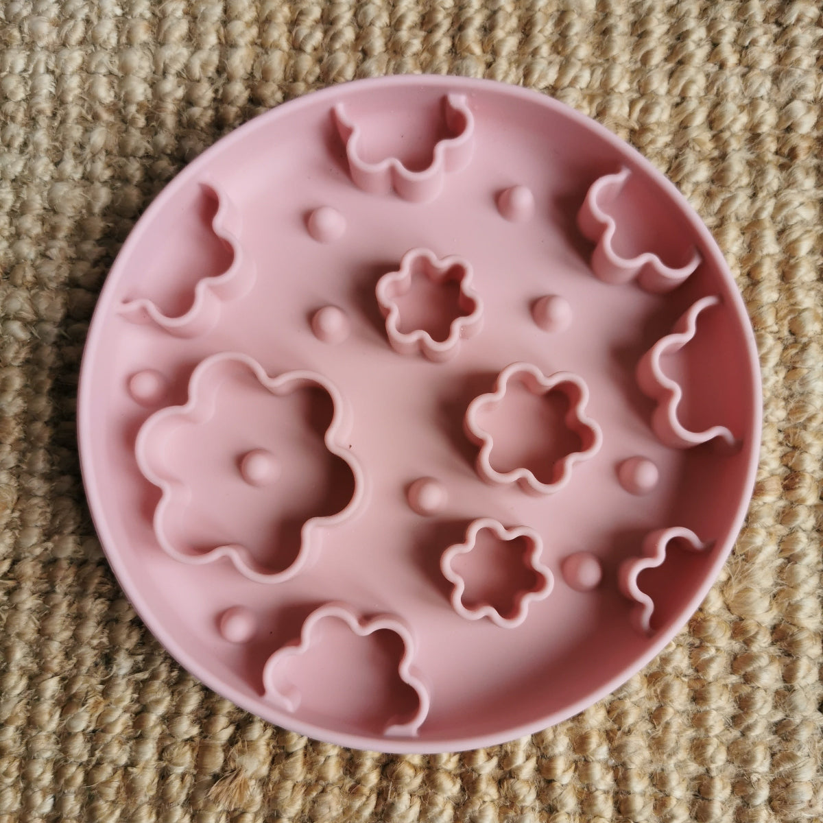 Pink silicone enrichment bowl with floral shapes on a textured surface