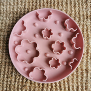 Pink silicone enrichment bowl with floral shapes on a textured surface