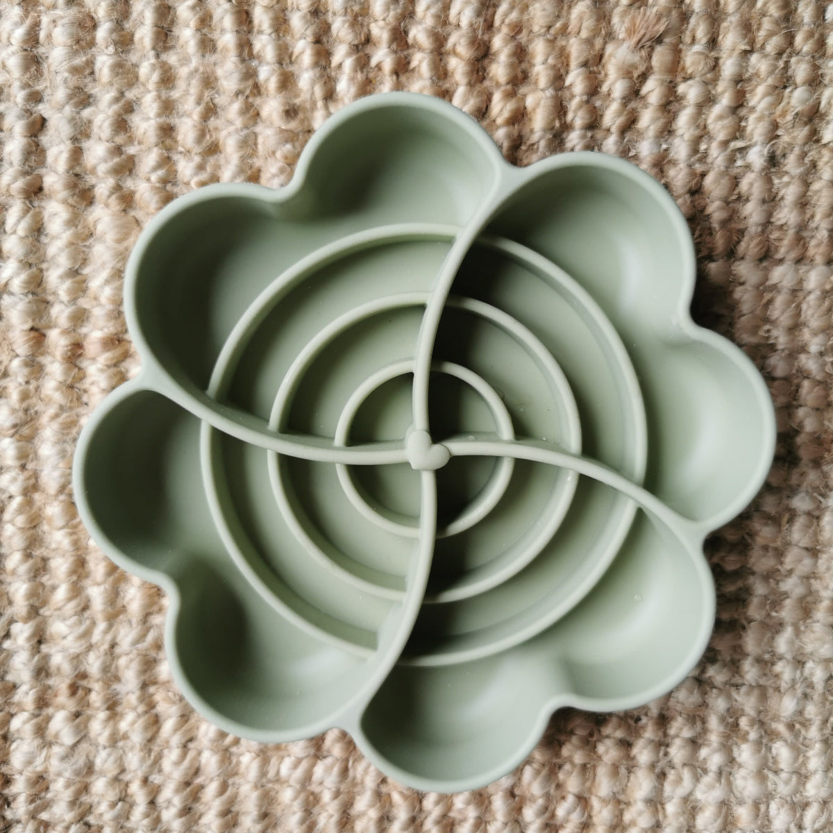 Green silicone flower-shaped enrichment bowl on a textured brown surface